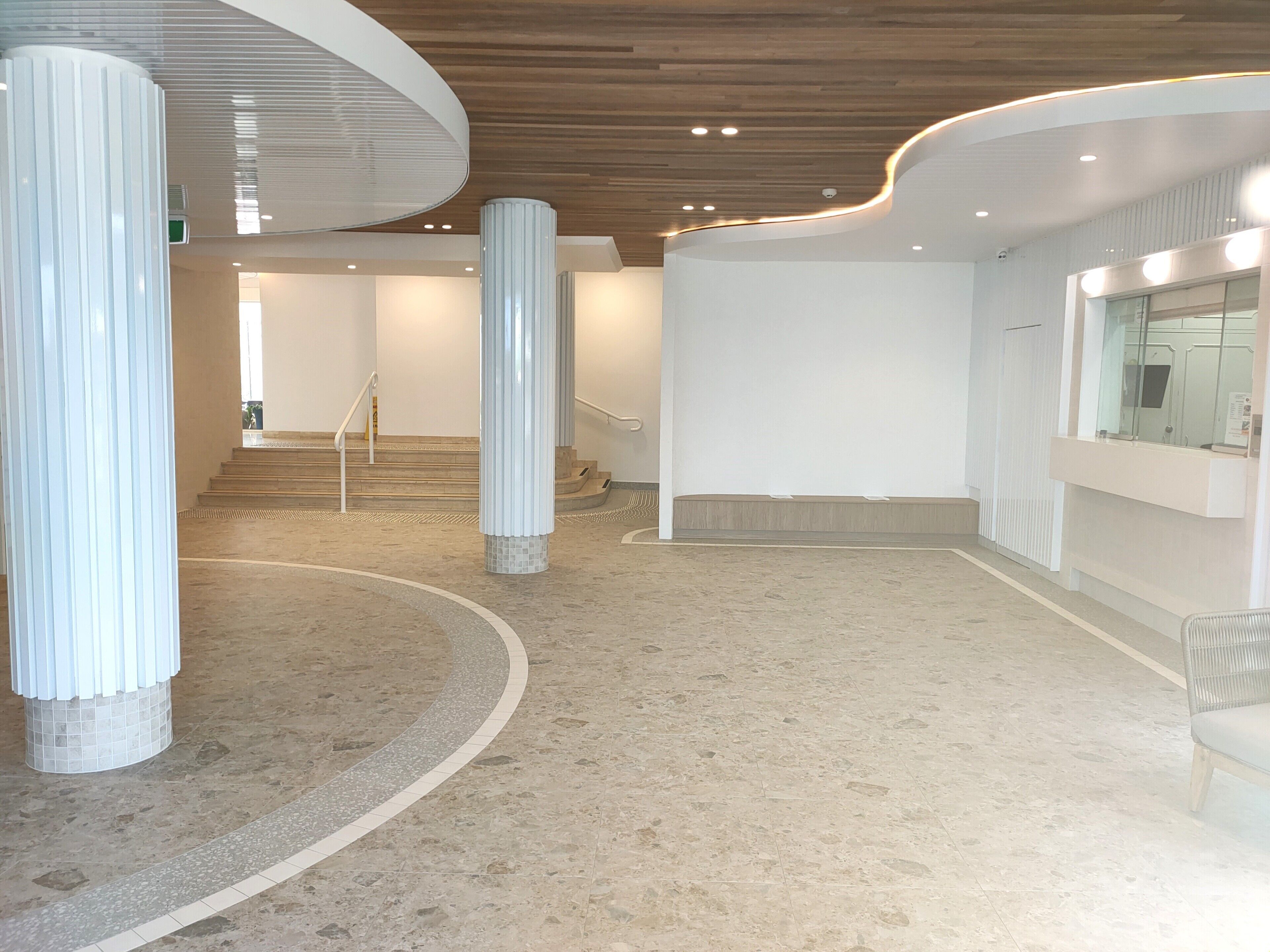 A spacious lobby with a curved floor, a staircase, and a reception area with a counter and a mirror.