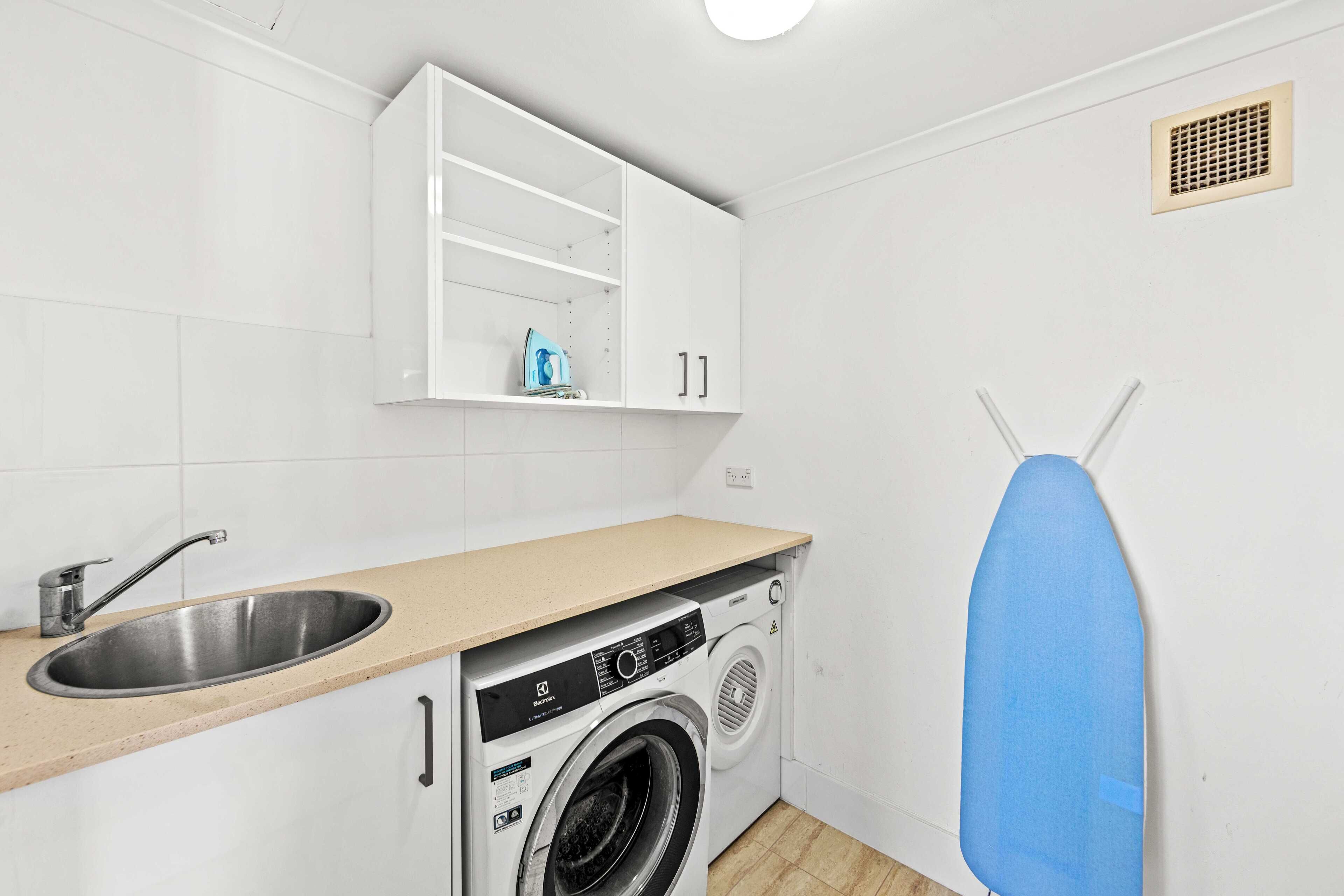 A compact laundry room with a washing machine, a sink, and a drying rack.