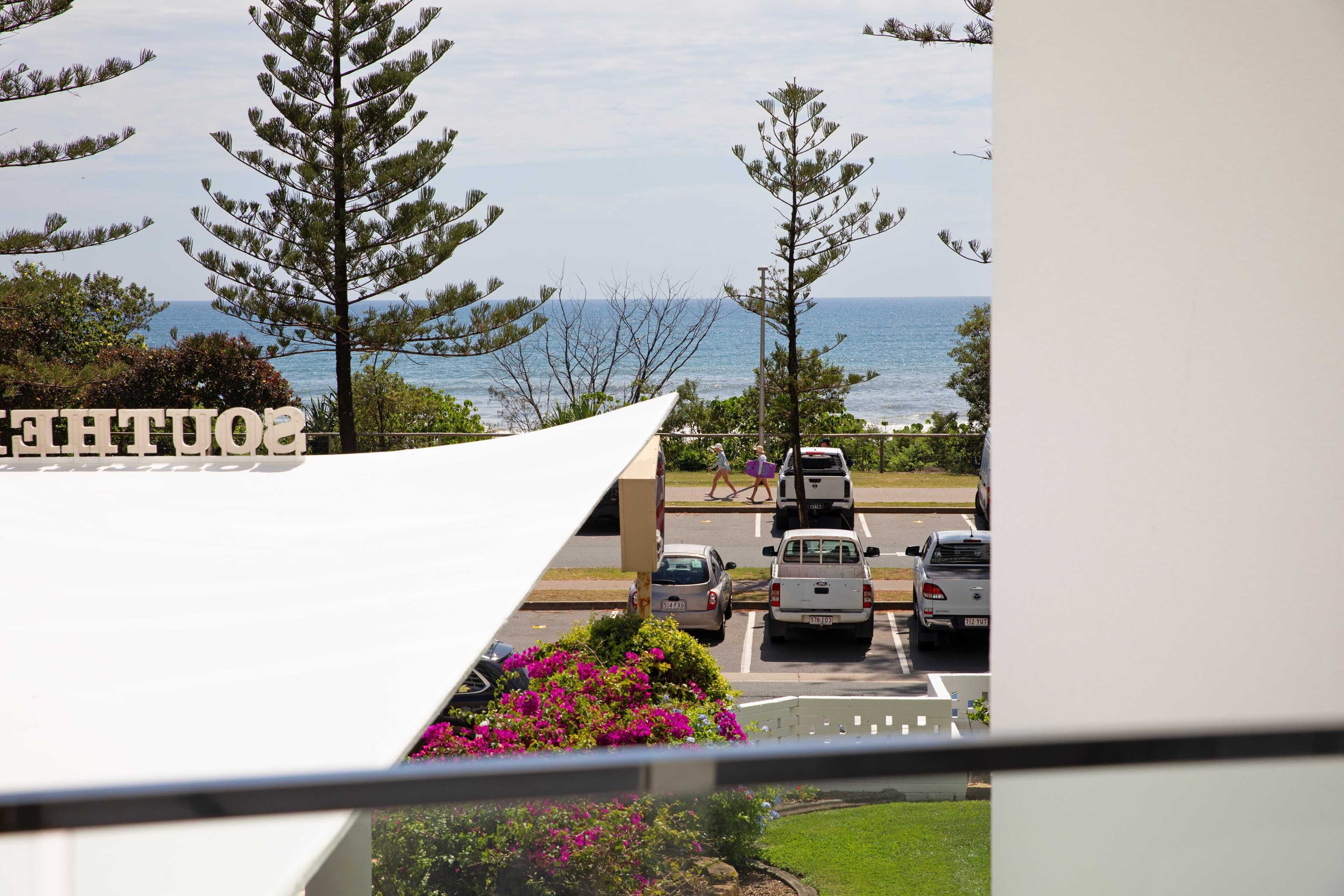 Un estacionamiento con vehículos, un edificio con un letrero y vista al mar.