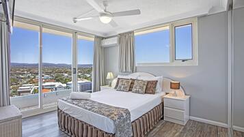 Ein Schlafzimmer mit einem großen Bett, einem Nachttisch, einem Deckenventilator und Blick auf eine Stadtlandschaft durch große Fenster.