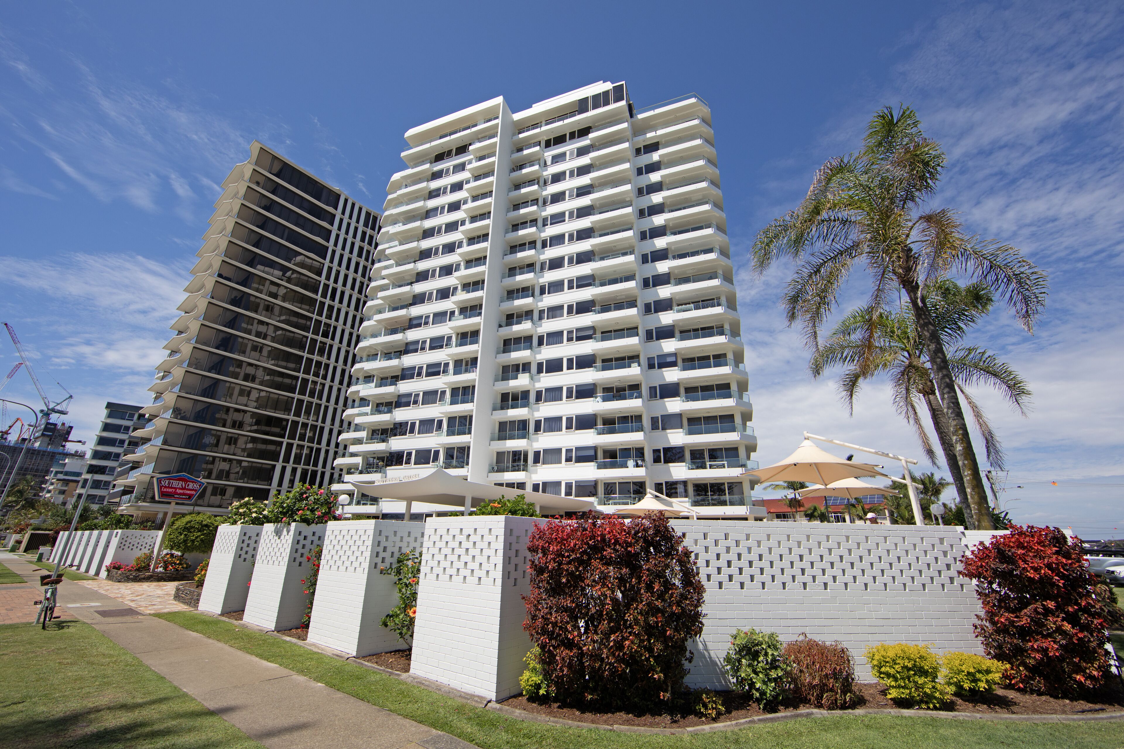 A modern high-rise hotel with multiple balconies, a well-maintained garden, and a clear view of the surrounding area.