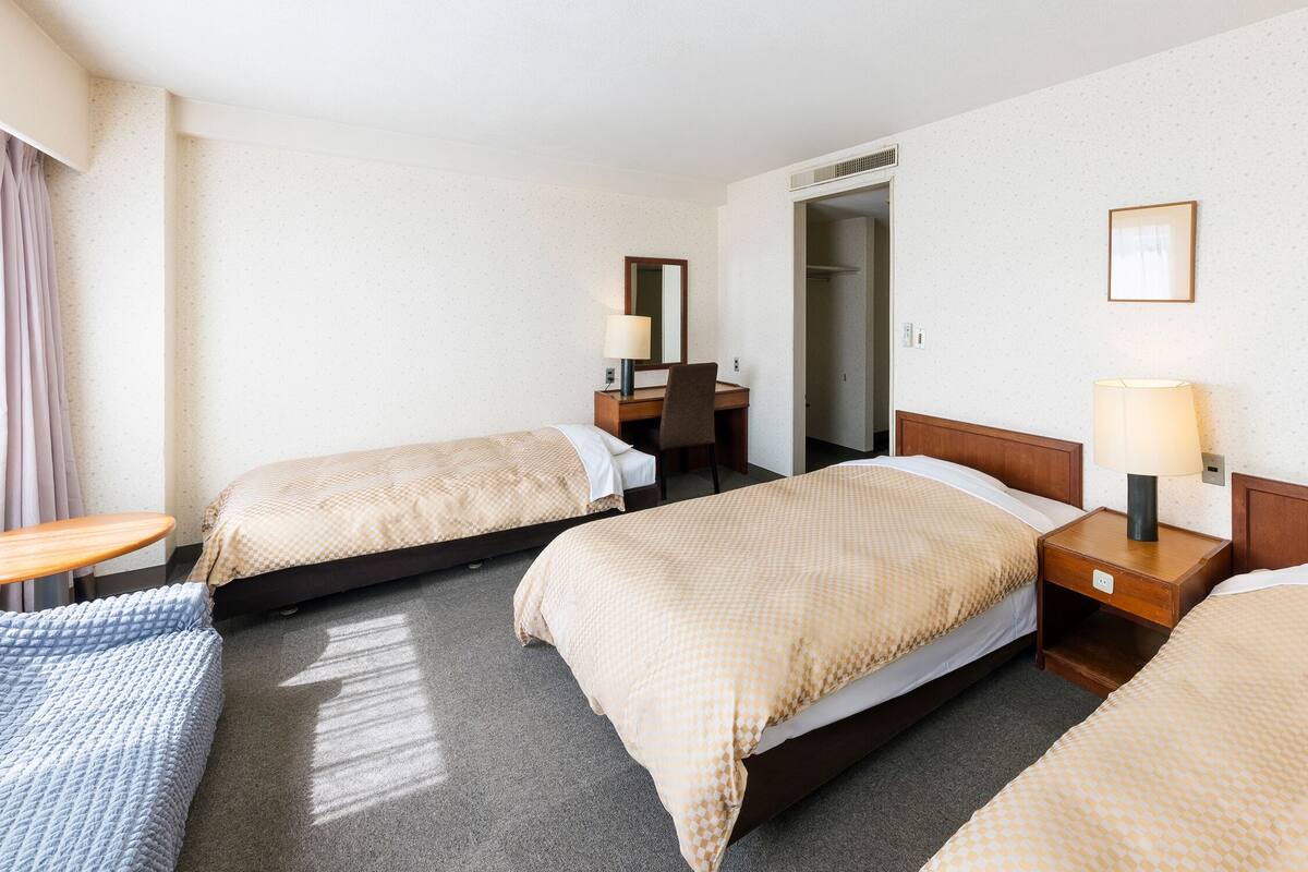 Ein Hotelzimmer mit zwei Betten, einem Schreibtisch, einem Stuhl, einer Lampe und einem Kleiderschrank.