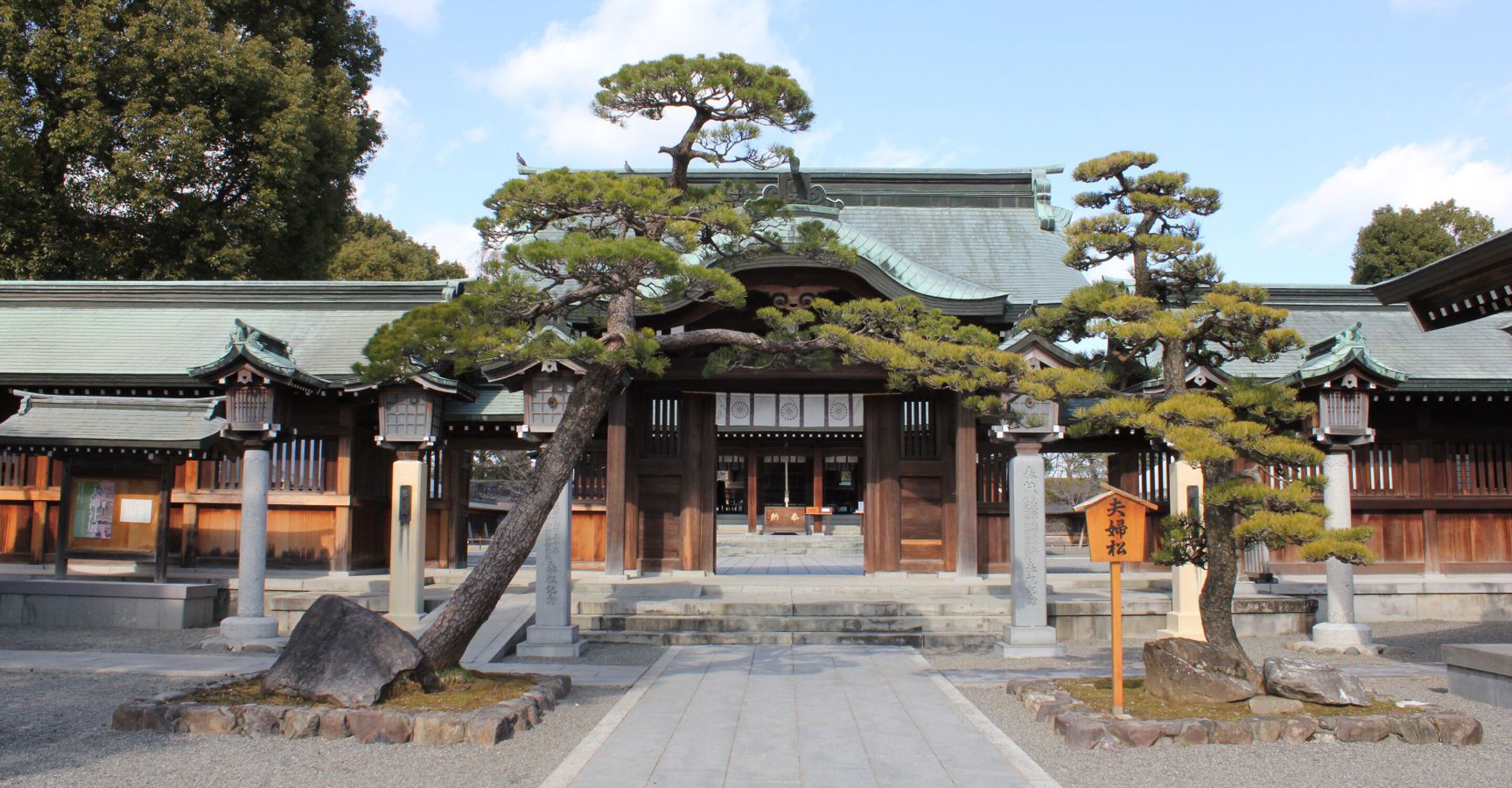 A traditional Japanese building with a central entrance, surrounded by stone lanterns and bonsai trees.