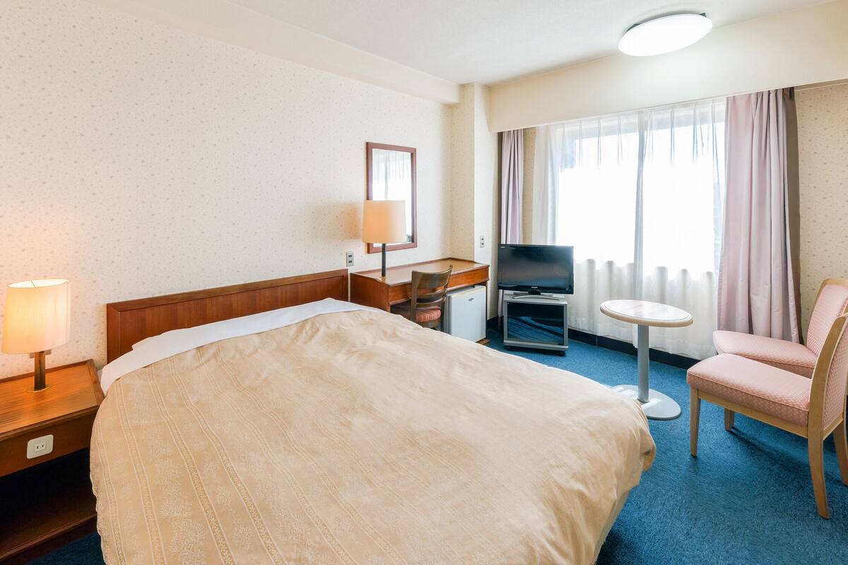 Ein Hotelzimmer mit einem Bett, einem Schreibtisch mit Fernseher, einem Sessel und einem kleinen Tisch.