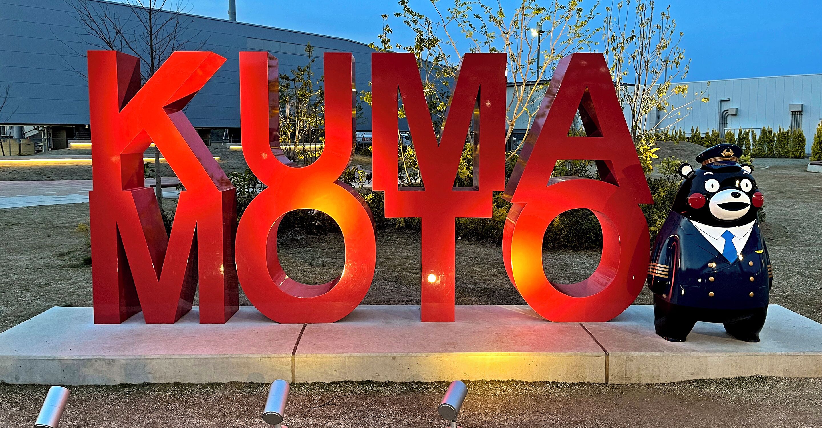 A large red sign with the letters "KUMA MOTO" and a bear mascot in a pilot uniform.