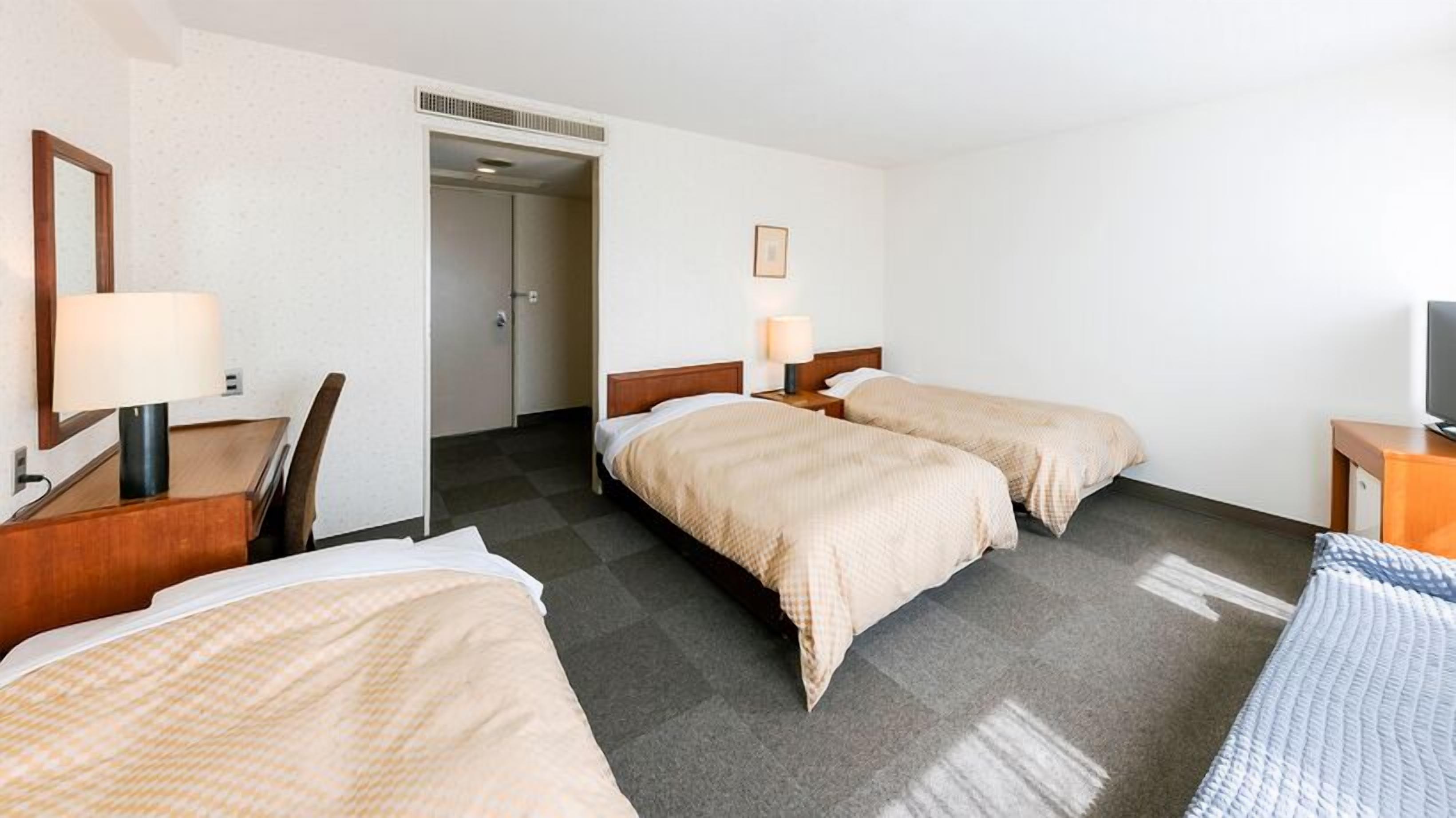 A hotel room with two beds, a desk, a chair, a TV, and a door leading to a bathroom.