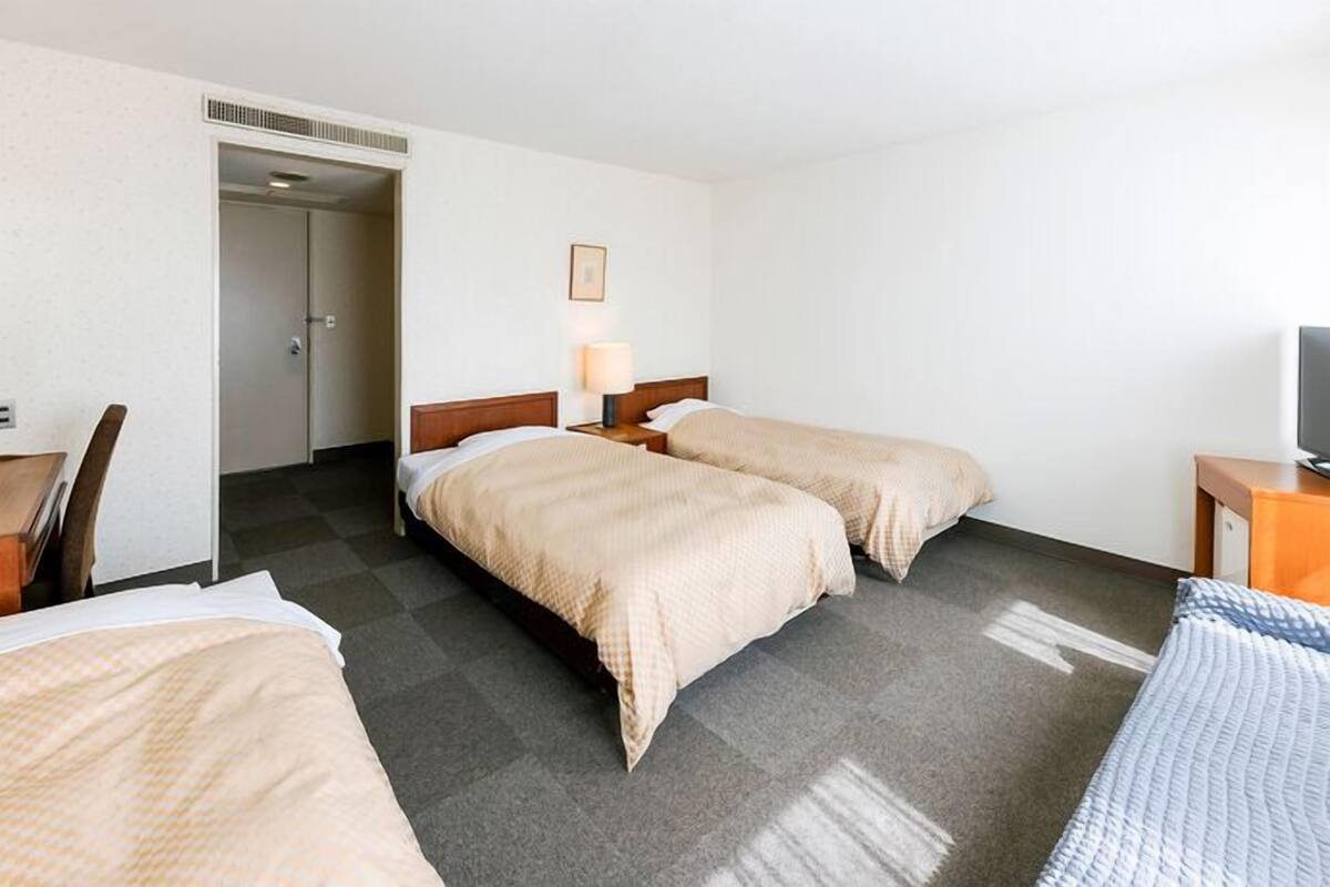 Ein Hotelzimmer mit zwei Betten, einem Schreibtisch, einem Stuhl, einem Fernseher und einer Tür zu einem Badezimmer.