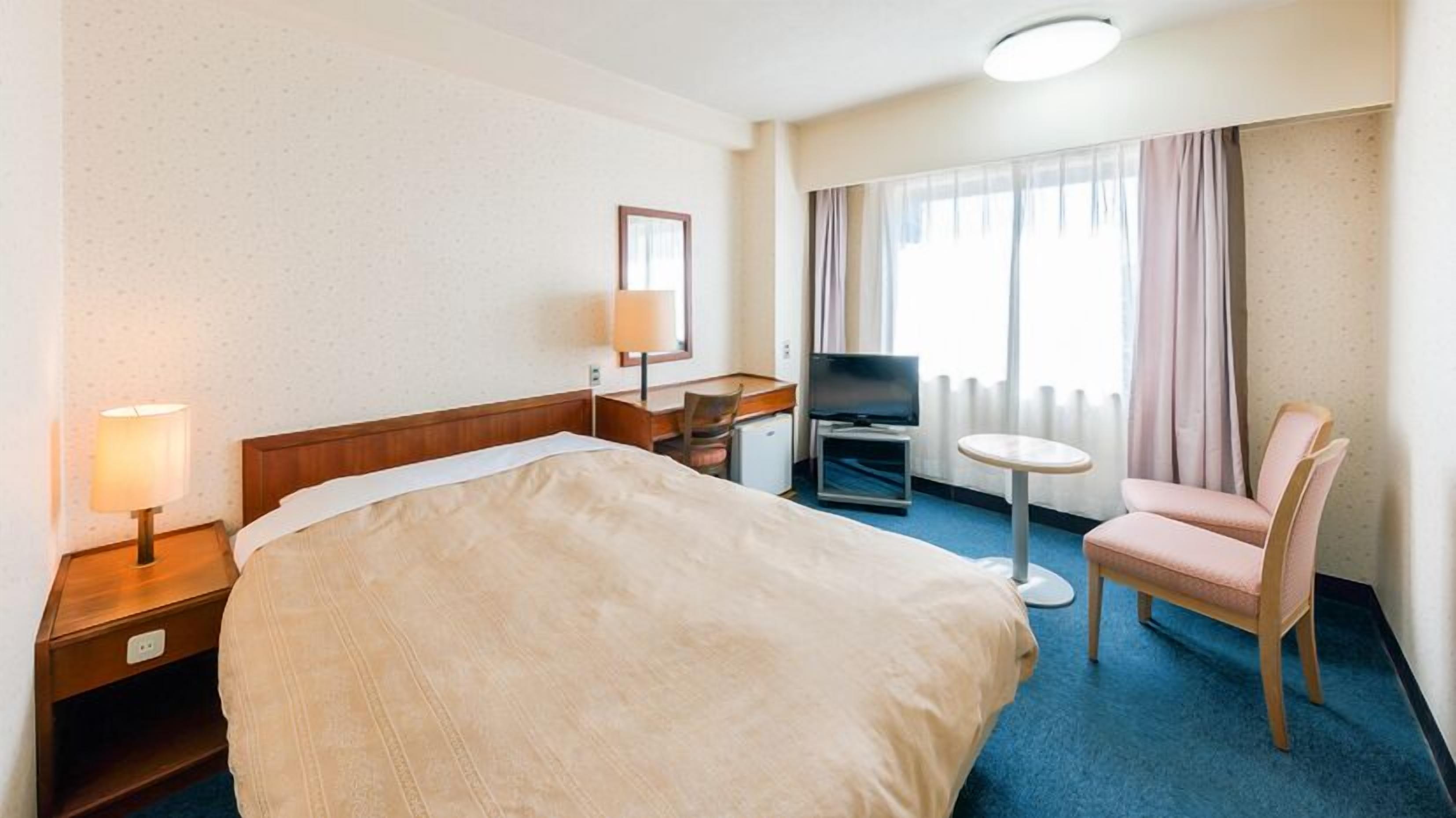 A hotel room with a bed, a desk, a chair, a TV, and a window with curtains.