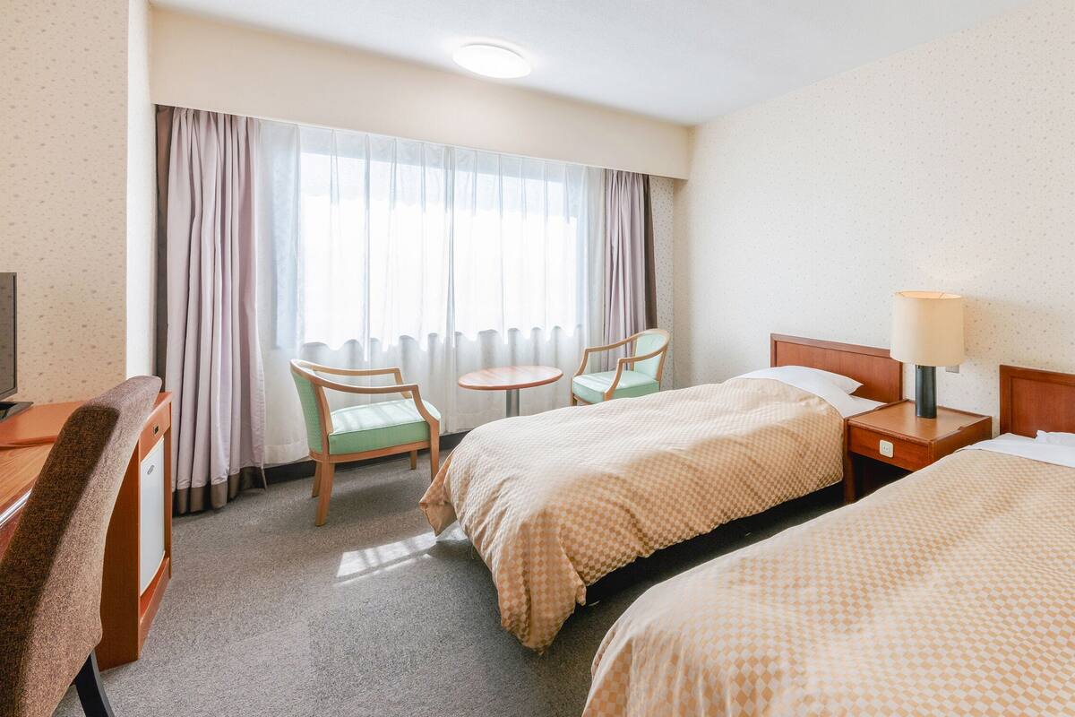 Ein Hotelzimmer mit zwei Betten, einem Schreibtisch, einem Stuhl, einem kleinen Tisch und einer Lampe.
