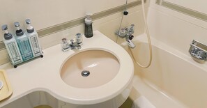 A bathroom with a sink, toilet, and bathtub. There are toiletries on the sink and a showerhead above the bathtub.