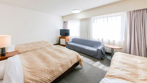 Hotelkamer met twee bedden, een televisie, een bank, een eettafeltje en een raam met gordijnen.