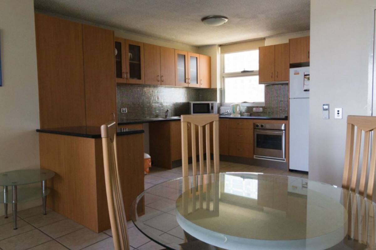 A kitchen with wooden cabinets, a glass table, and a small round table.