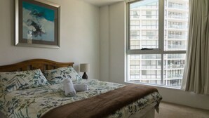 A hotel room with a bed, a painting on the wall, a window with curtains, and a view of a building outside. - Durham Court Holiday Apartments (Surfers Paradise)