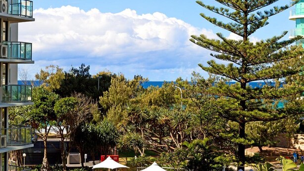 A multi-story building with balconies, surrounded by lush greenery and a clear sky. - Durham Court Holiday Apartments (Surfers Paradise)
