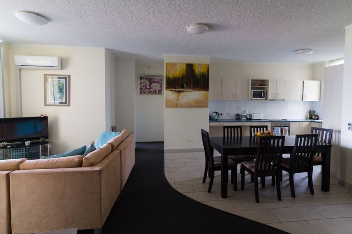 A modern living room with a sofa, a TV, and a dining area with chairs and a table.