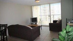 A living room with a sofa, a TV, and a large window with blinds. - Durham Court Holiday Apartments (Surfers Paradise)