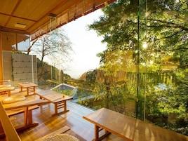 Uma área de estar ao ar livre com mesas e bancos de madeira, com vista para um jardim e um edifício com telhado inclinado.