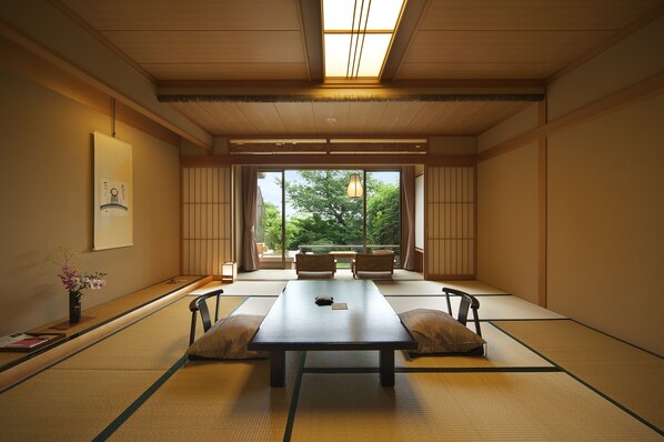 Una habitación tradicional japonesa con tatami, una mesa baja, cojines y vistas a la vegetación exterior.