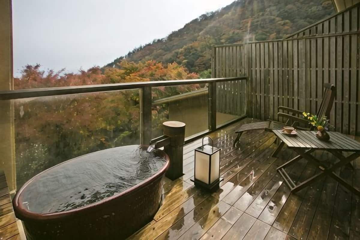 A wooden deck with a hot tub, a table with flowers, and a view of autumn foliage.