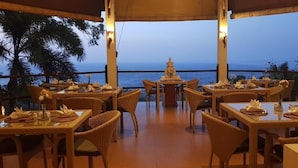 Un área de comedor al aire libre con mobiliario de mimbre y mesas dispuestas para la cena, con vista al océano.