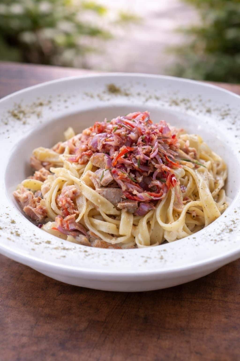A plate of pasta with a topping of red onions and herbs.