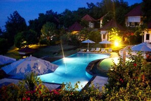 A swimming pool with lounge chairs and umbrellas, surrounded by greenery and buildings with red roofs. - The Hamsa Bali Resort (Banjar)