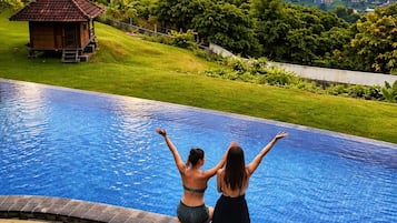 Una piscina con dos personas sentadas en el borde, mirando un cuerpo de agua y un edificio pequeño.
