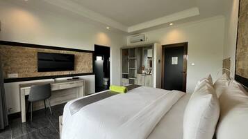 Une chambre d’hôtel moderne, dotée d’un grand lit, d’un bureau avec une chaise, d’un téléviseur à écran plat fixé au mur et d’une salle de bain visible à travers une porte ouverte.