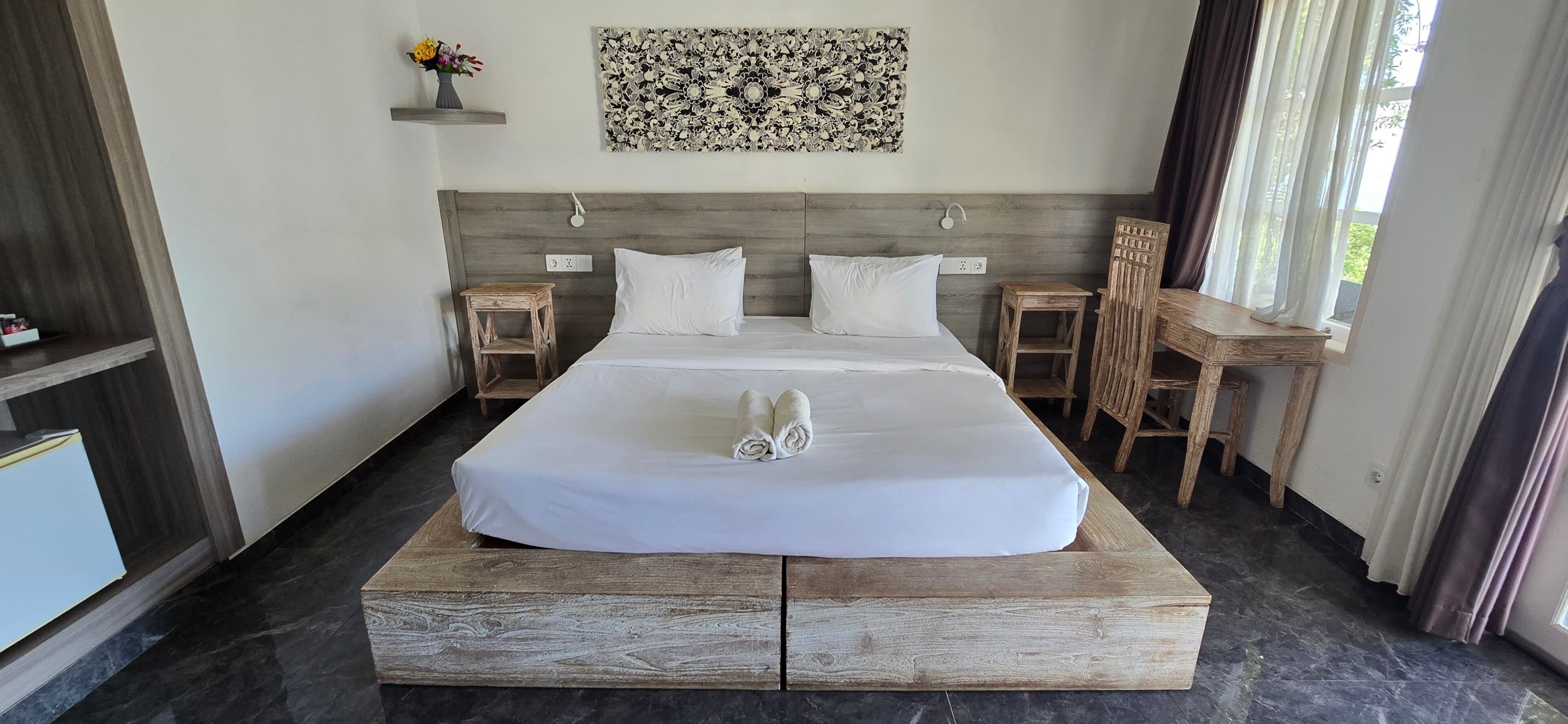 A hotel room with a large bed, a wooden headboard, a small table, a chair, and a wall-mounted artwork.