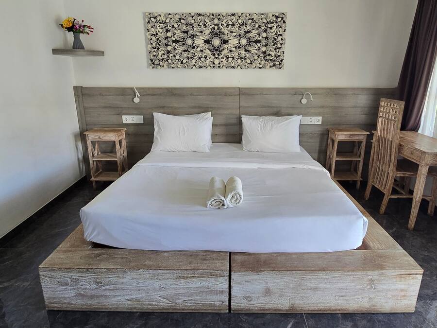A hotel room with a large bed, a wooden headboard, a small table, a chair, and a wall-mounted artwork.