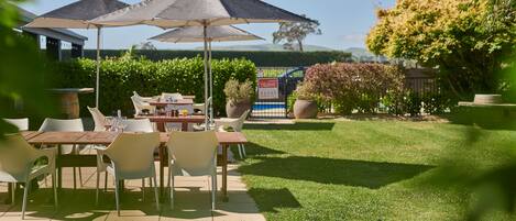 An outdoor patio with tables and chairs, umbrellas, and a well-maintained lawn.