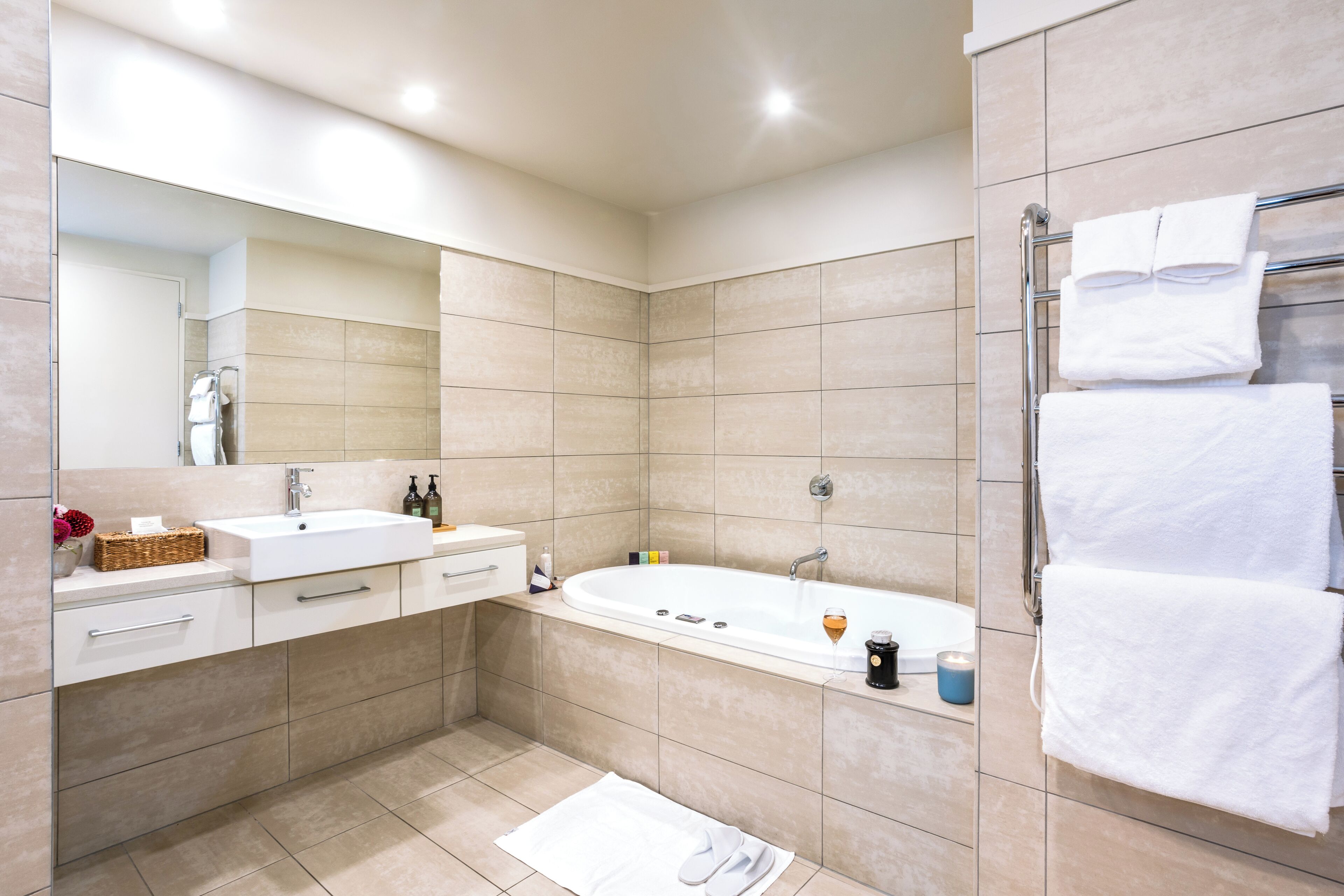 A modern bathroom with a large bathtub, two sinks, a vanity with drawers, and a towel rack.