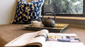 A room with a window, a patterned pillow, a tray with a teapot and cup, and an open magazine.