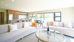 A modern living room with a sofa, a glass coffee table, and a kitchen area with a refrigerator and cabinets. - Parehua Resort (Martinborough)