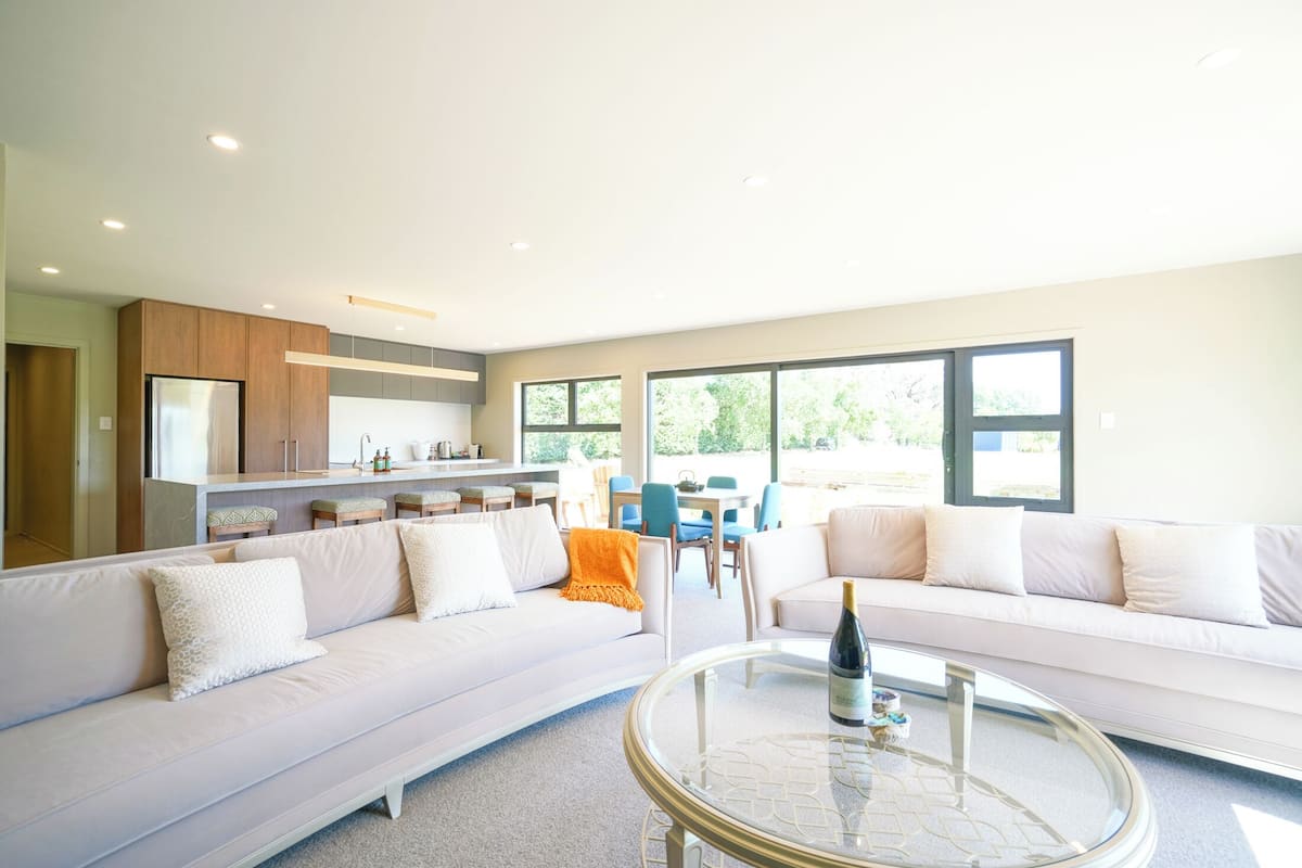 A modern living room with a sofa, a glass coffee table, and a kitchen area with a refrigerator and cabinets.