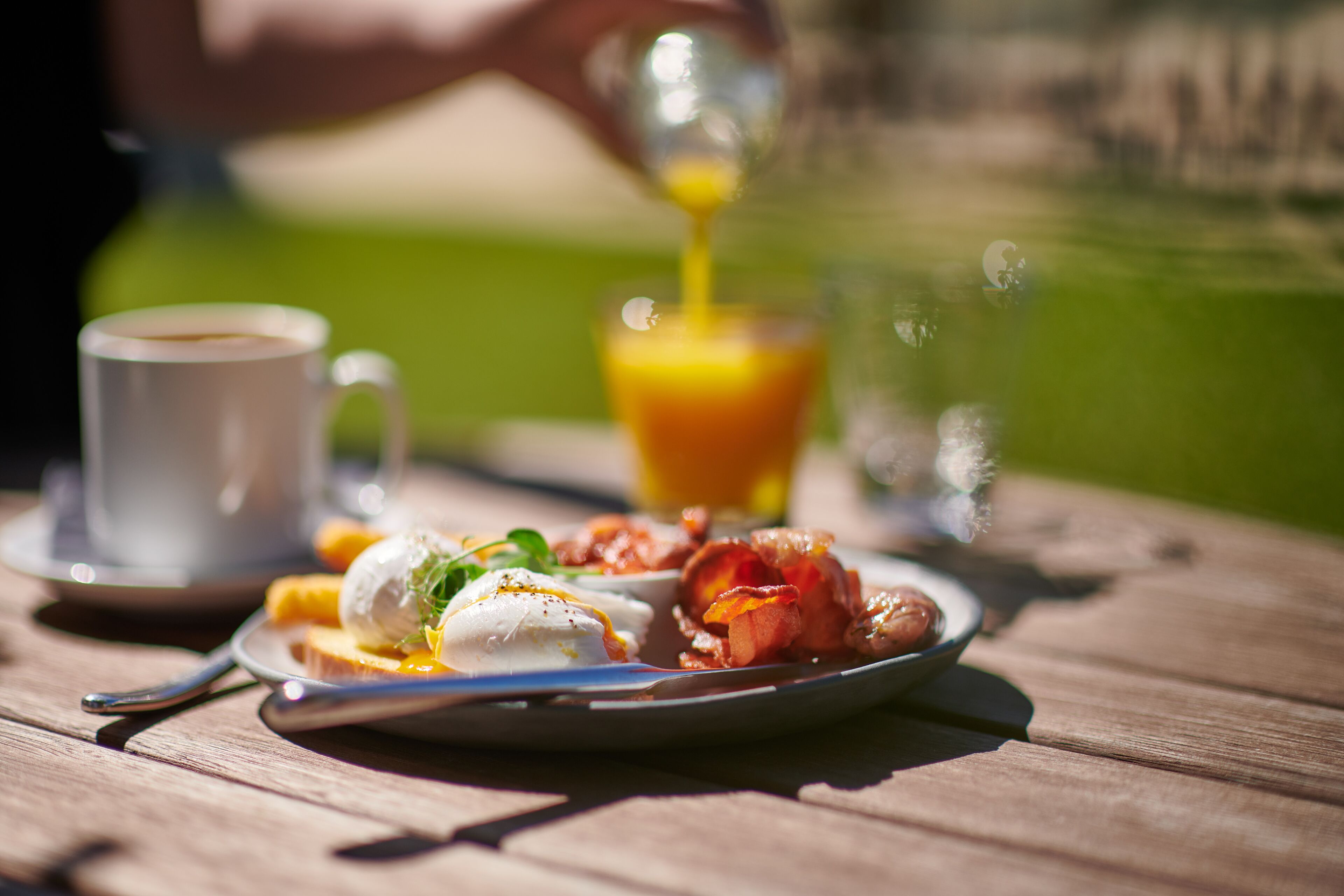 A breakfast setting with a plate of food, a cup of coffee, and a glass of orange juice on a wooden table.