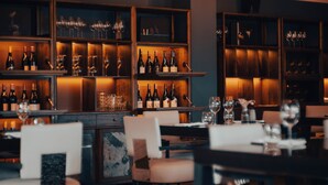 A restaurant with wooden shelves displaying wine bottles and glasses, and tables with chairs set for dining. - Parehua Resort (Martinborough)