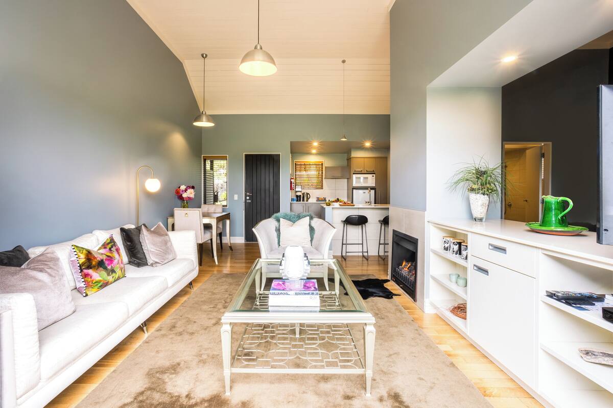A modern living room with a glass coffee table, white sofa, and a kitchen in the background.