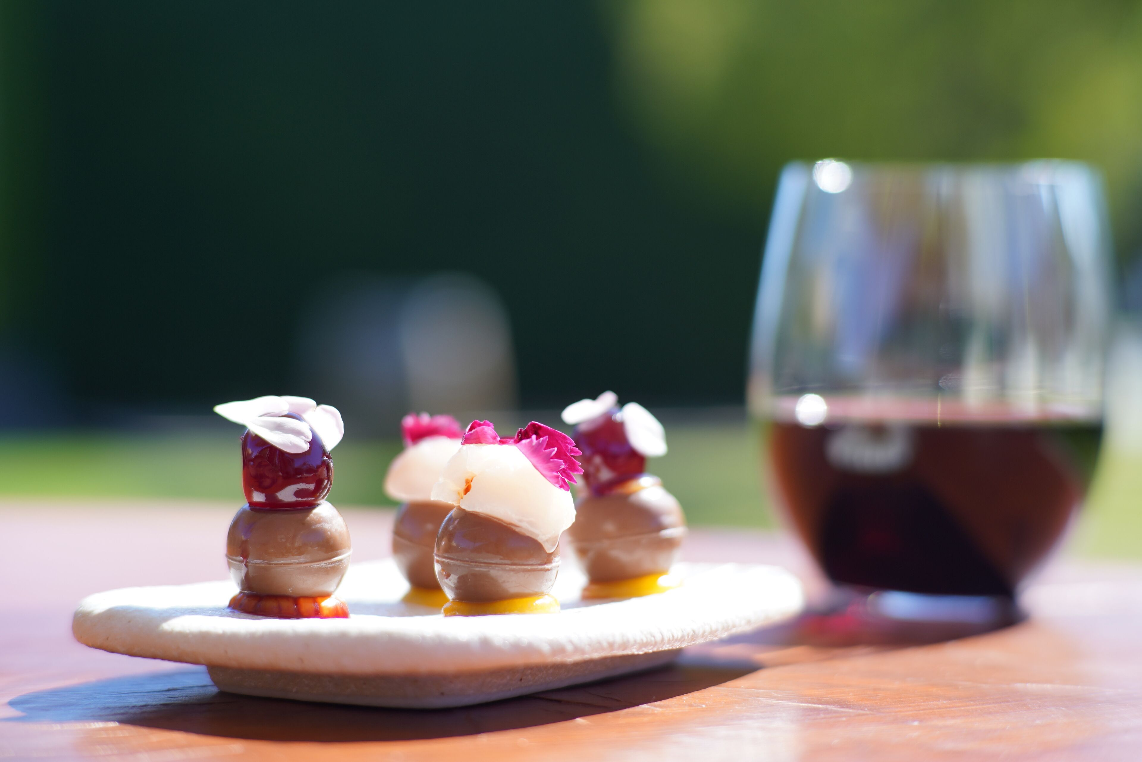 A dessert plate with three spherical treats, a glass of dark liquid, and a blurred green background.