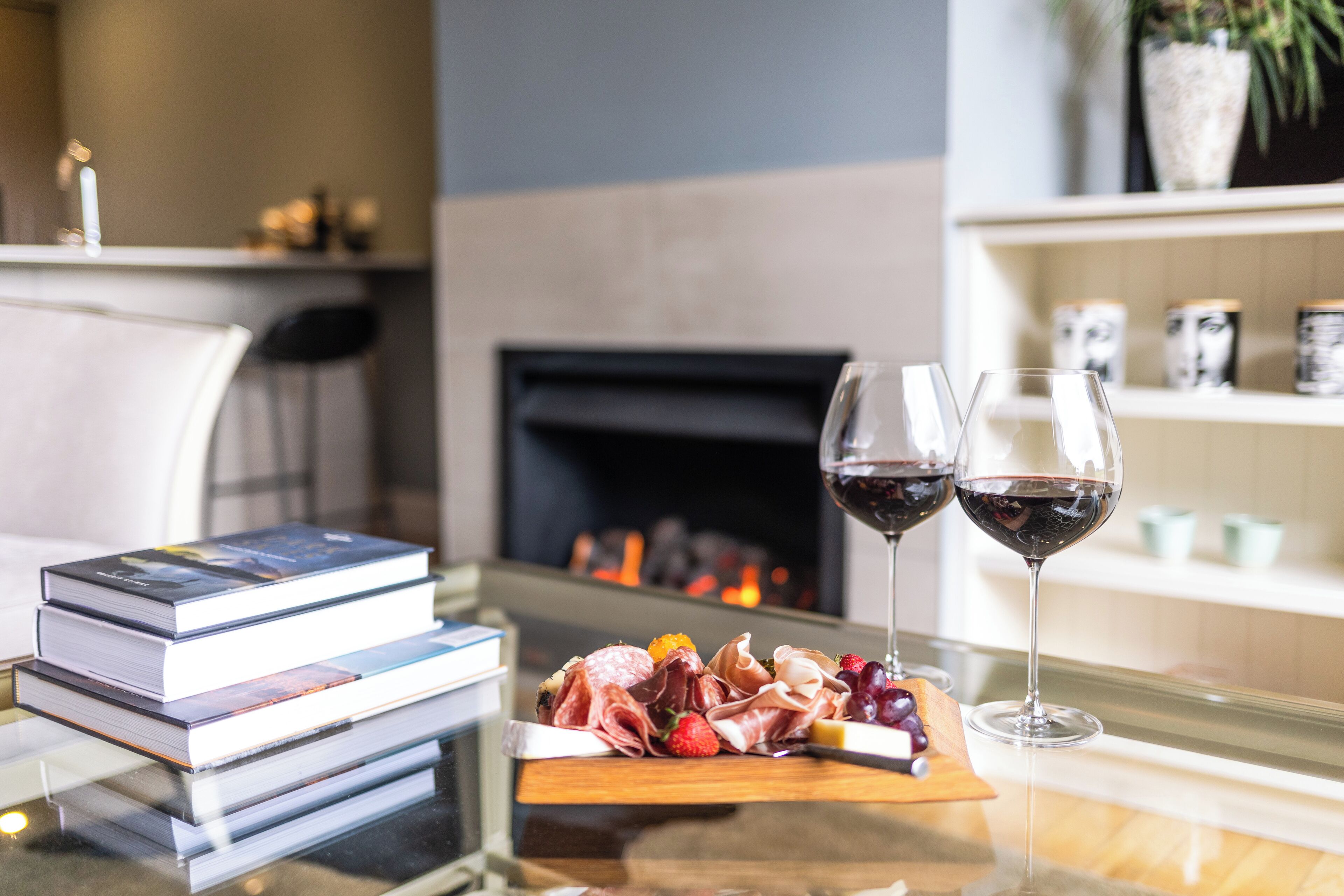 A table with a book stack, a charcuterie board, and two glasses of red wine.