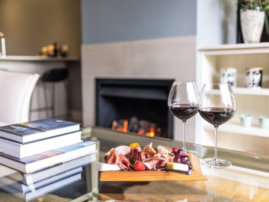 A table with a book stack, a charcuterie board, and two glasses of red wine.