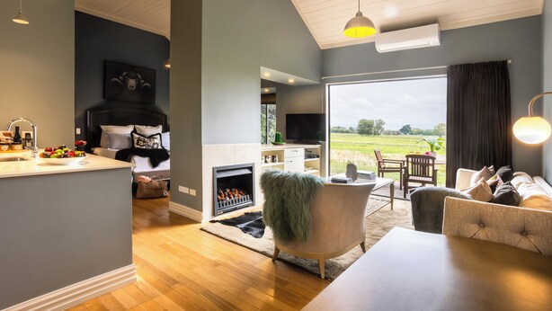 A modern living room with a fireplace, a dining area, and a view of the outdoors. - Parehua Resort (Martinborough)