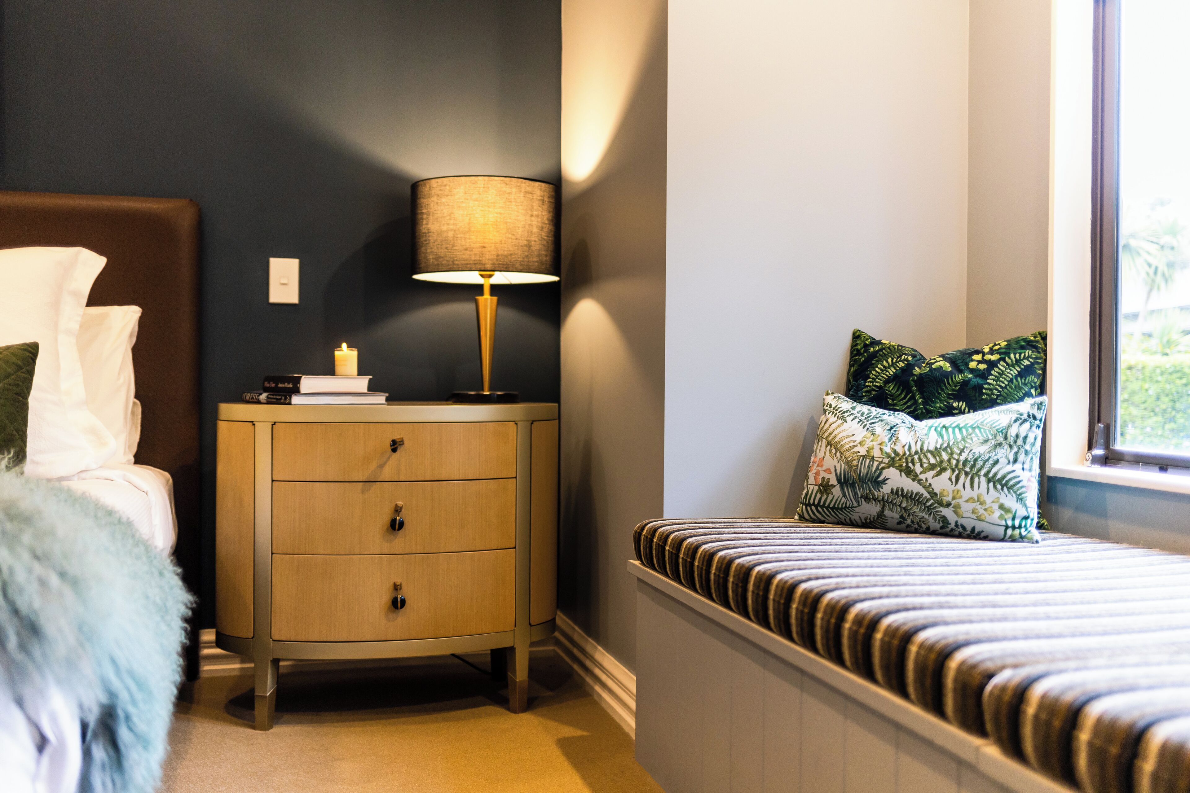 A bedroom with a bed, a nightstand with a lamp, and a window with a view.