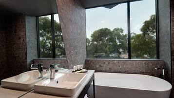 Casa de banho moderna com duas pias, banheira e uma janela ampla com vista para árvores.