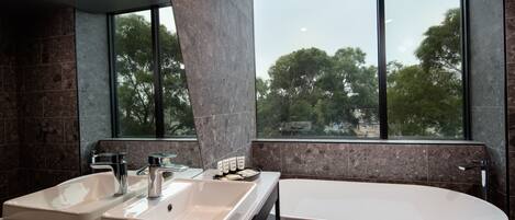 Un baño moderno con dos lavamanos, una bañera y un amplio ventanal con vistas a árboles.