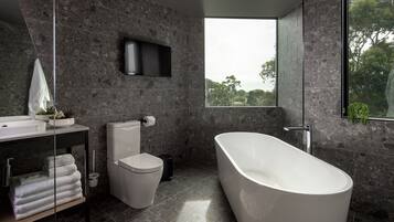 A modern bathroom with a freestanding bathtub, a toilet, a sink, and a large window offering a view of trees.
