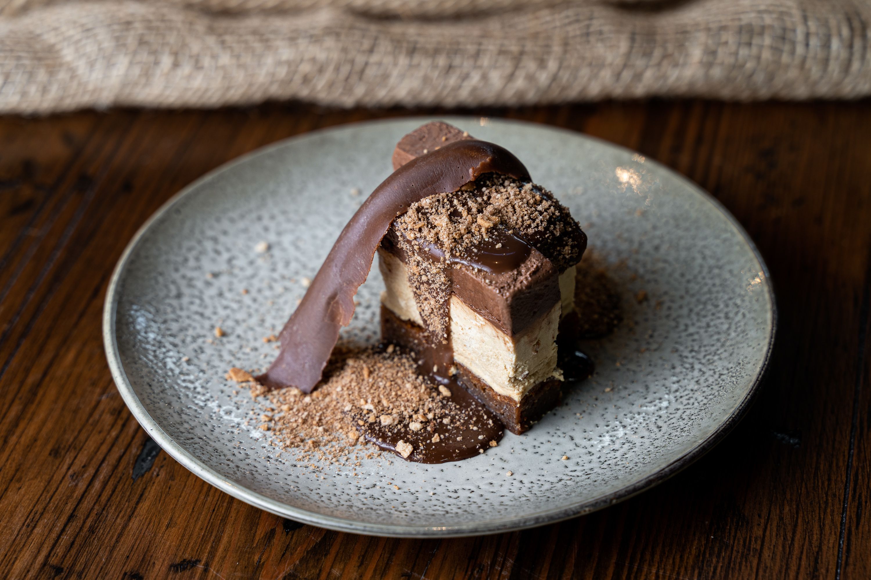 A dessert on a plate with a chocolate drizzle and crumbs on top.