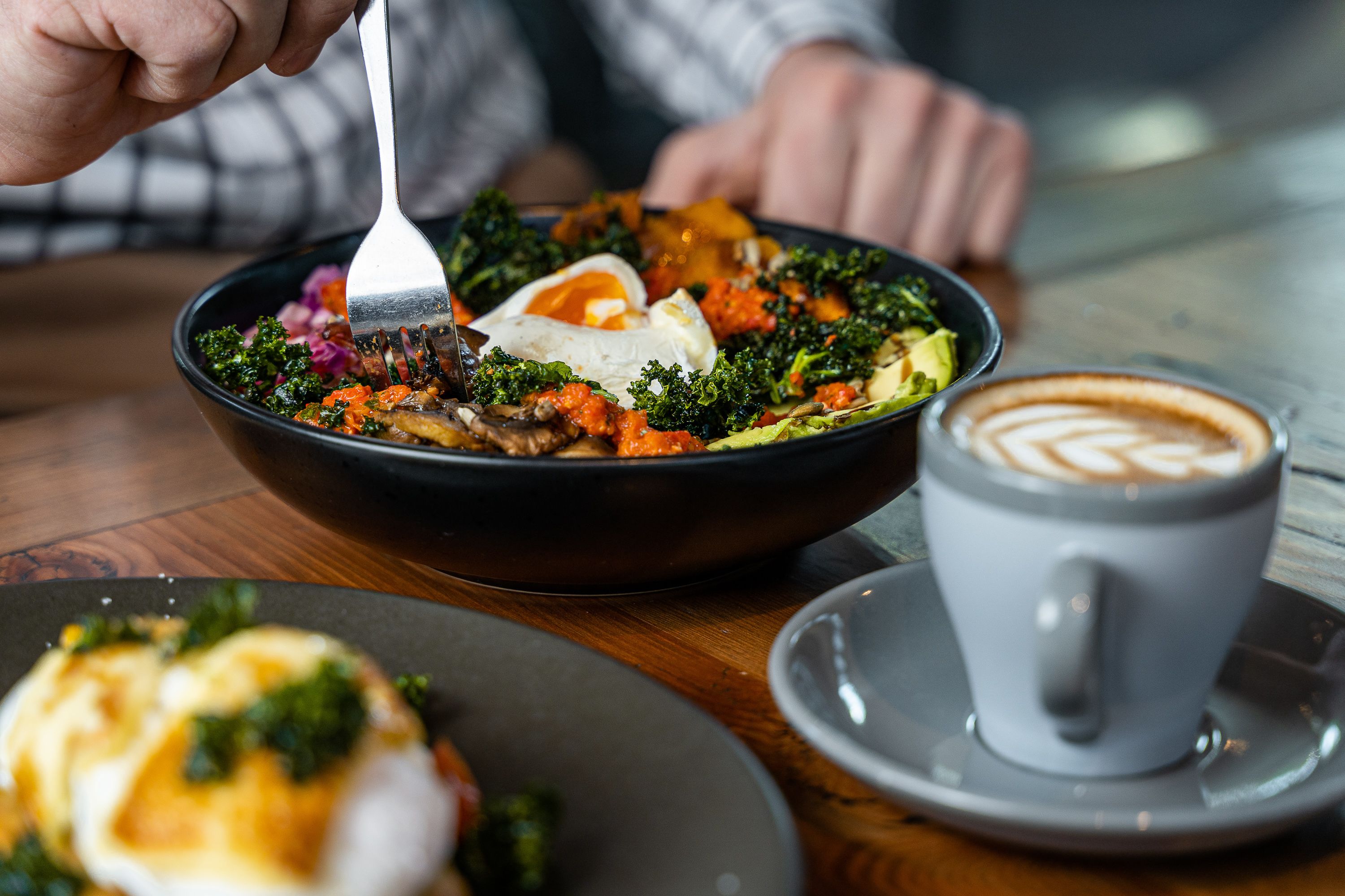 Un bol de nourriture avec une fourchette, une tasse de café et une assiette avec une pâtisserie.