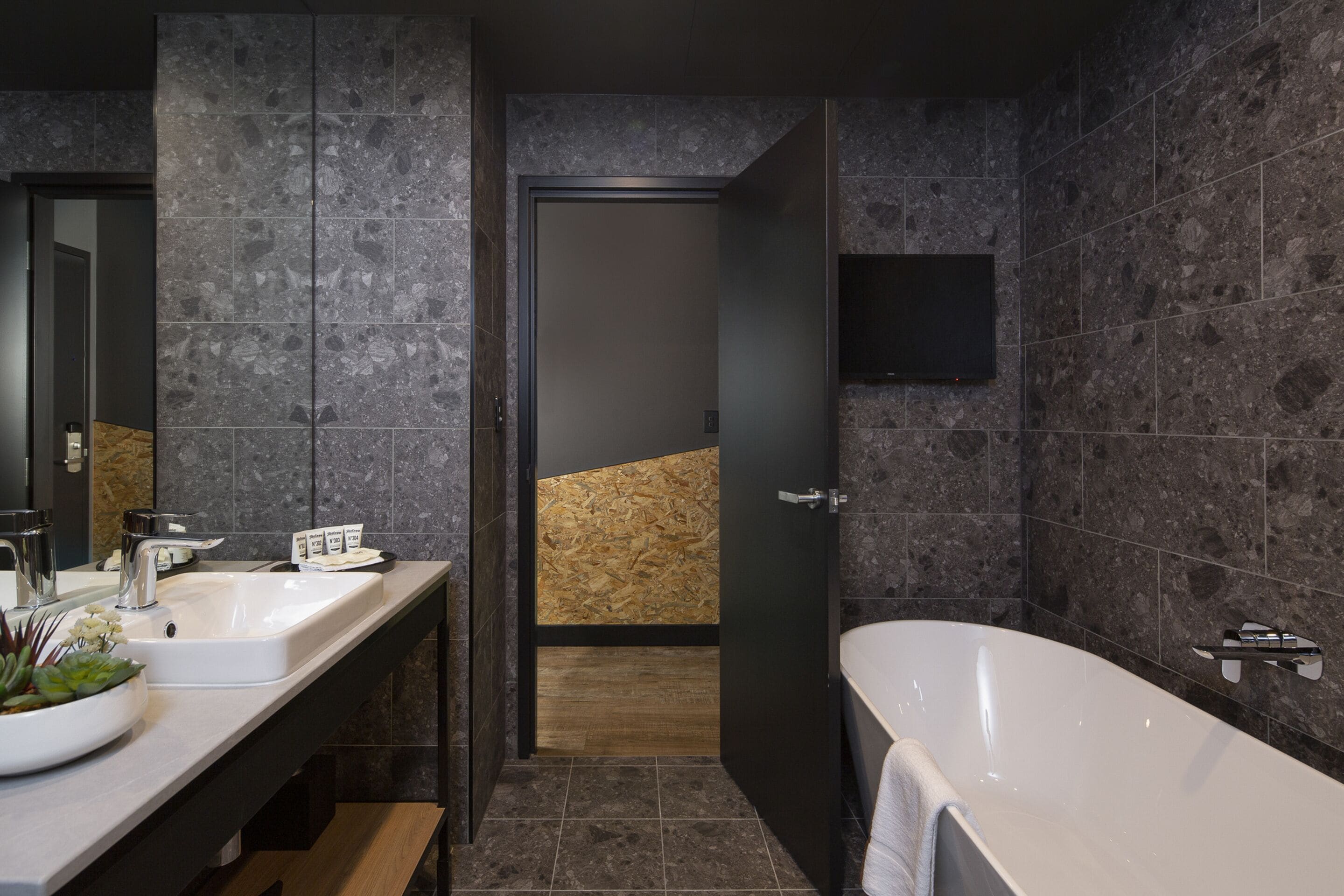Een moderne badkamer met twee wastafels, een ruim bad en een wand van houten panelen.