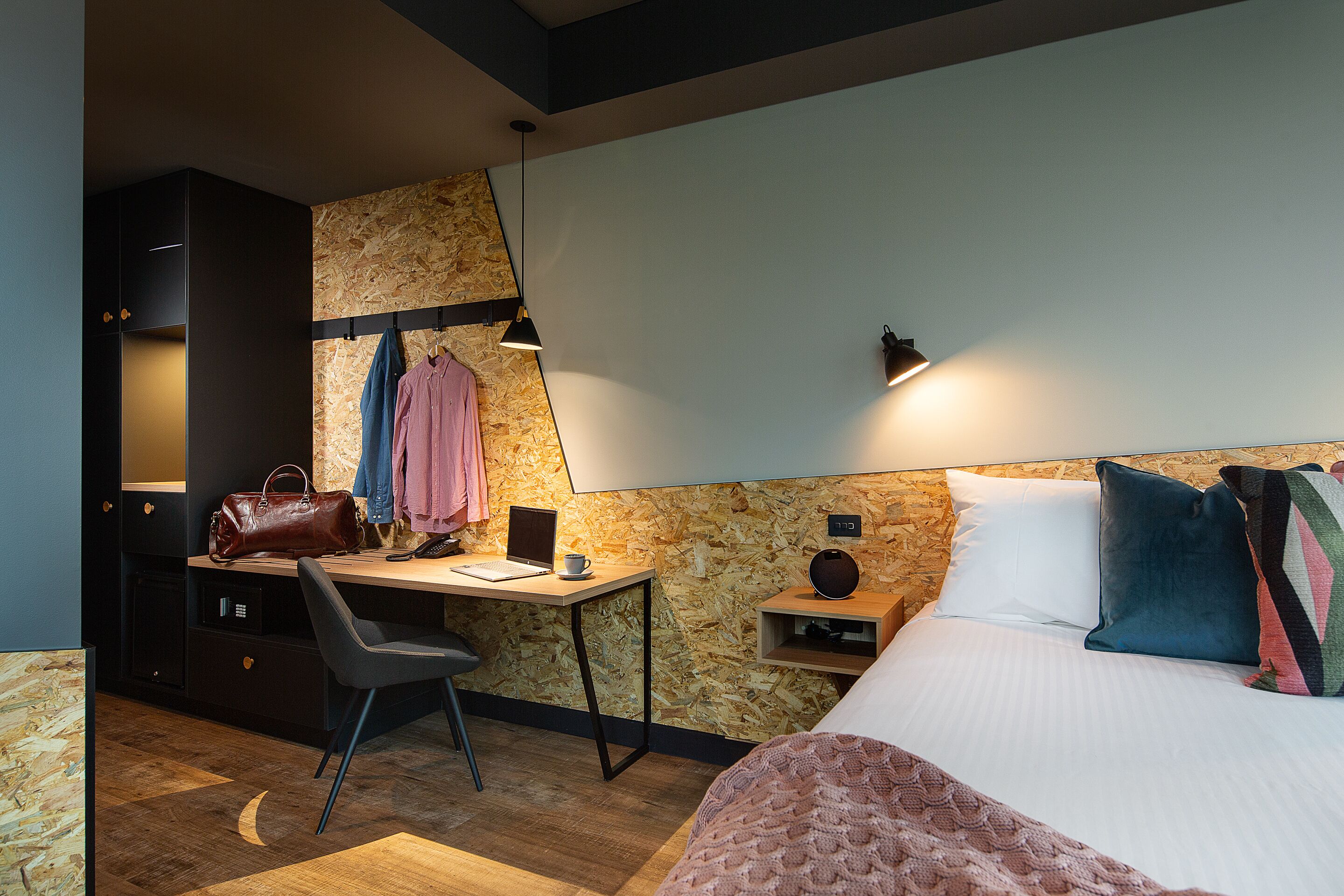 A bedroom with a bed, bedside table, desk, chair, and a wardrobe.